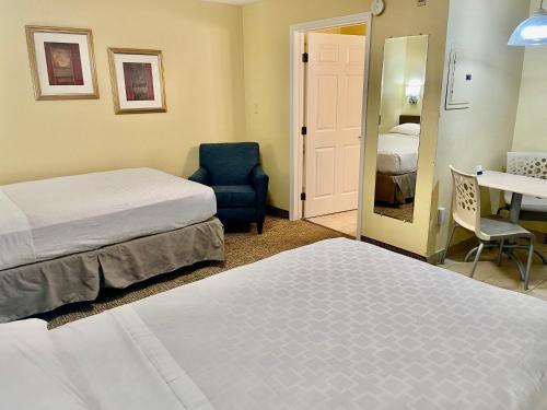 a hotel room with two beds and a chair and a mirror at Suburban Studios Fort Myers Cape Coral in Fort Myers