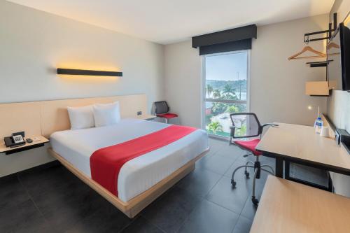 a hotel room with a bed and a desk and a window at City Express by Marriott Paraiso in Paraíso