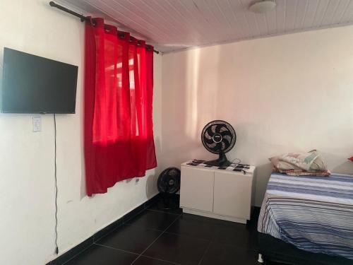 a room with a red curtain and a bed and a tv at Kit net linda e aconchegante in Cabo Frio