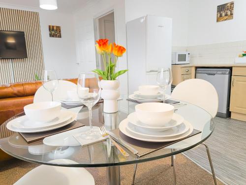 a dining room with a glass table with white plates and flowers at Deluxe 2-bed Apartment, Family friendly, Free Parking, Netflix & Amazon Prime Video Streaming in Farnworth