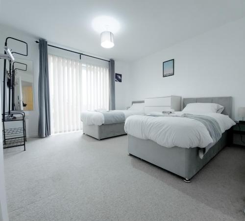 a white bedroom with two beds and a window at Deluxe 2-bed Apartment, Family friendly, Free Parking, Netflix & Amazon Prime Video Streaming in Farnworth