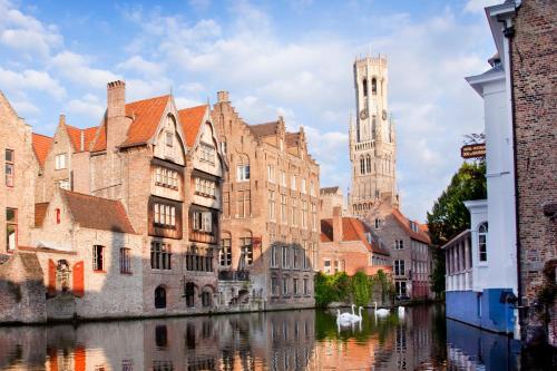 a group of buildings next to a river with a clock tower at Aragon House in Bruges