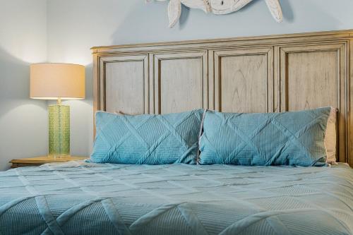 a bed with blue pillows and a wooden headboard at Lovely Resort Low Floor Condo! Just Steps to the Beach & Restaurants! by Dolce Vita Getaways PCB in Panama City Beach