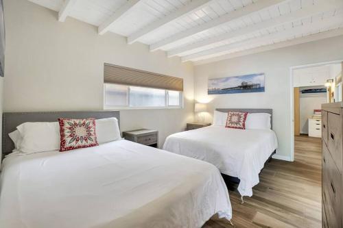 two beds in a bedroom with white walls and wood floors at ON THE SAND!! Private Beach! OCEAN FRONT HOT TUB!! in Dana Point