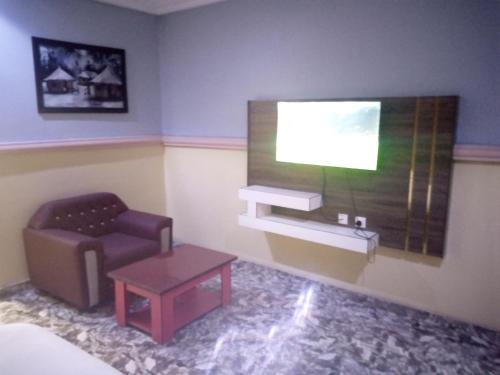 Habitación con silla y TV en la pared. en De Jacob's Hotel & Suites en Umunya