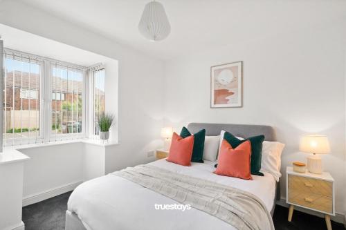 a white bedroom with a bed with orange and green pillows at 1 Sarah House by Truestays - 2 Bedroom Apartment - FREE Wifi & Parking in Manchester