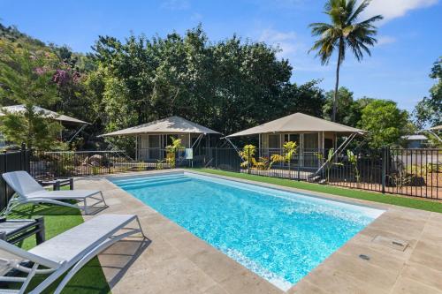 a swimming pool with chairs and a fence and trees at Deluxe King Safari Tent 2 in Nelly Bay
