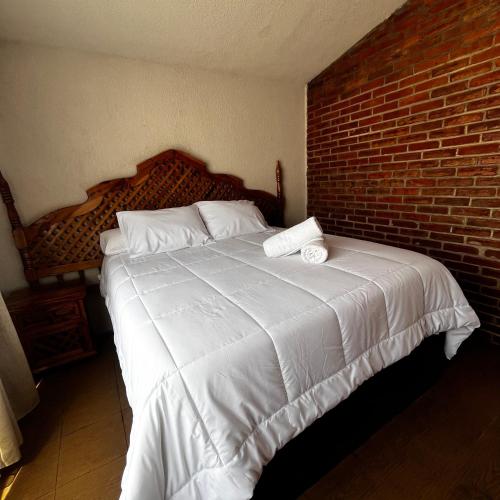 1 dormitorio con 1 cama blanca grande y pared de ladrillo en La Cabaña de Don Neto en Santa María Atlihuetzián