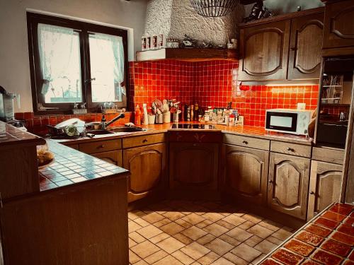 a kitchen with wooden cabinets and a red tiled wall at La Croisée des Chemins 