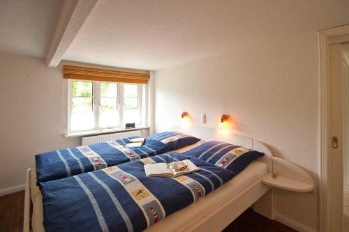 a bedroom with a bed with blue sheets and a window at Suetjers-Wenang in Süddorf