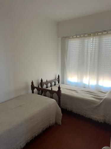 a white bedroom with two beds and a window at Departamento céntrico in Monte Hermoso