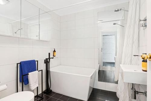 Baño blanco con bañera y lavamanos en Halifax Muse Pet Friendly Townhouse, en Adelaida