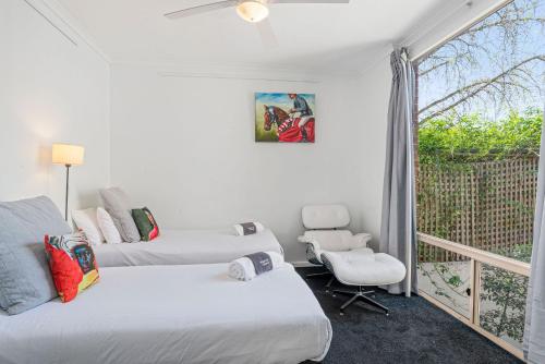 a bedroom with two beds and a chair and a window at Halifax Muse Pet Friendly Townhouse in Adelaide