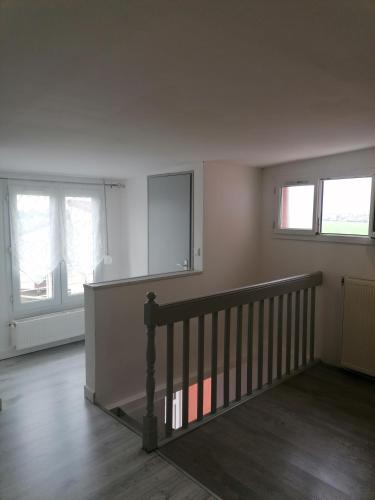 una stanza vuota con una scala e due finestre di Appartement moderne a Rouvroy