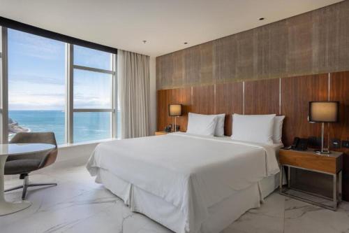 um quarto com uma grande cama branca, uma secretária e uma janela. em Hotel Nacional no Rio de Janeiro