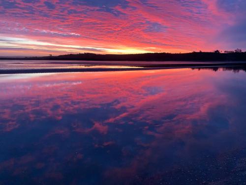 a sunset on the beach with clouds in the water at Pukehina Estuary Sunset Views Townhouse & Studio in Pukehina