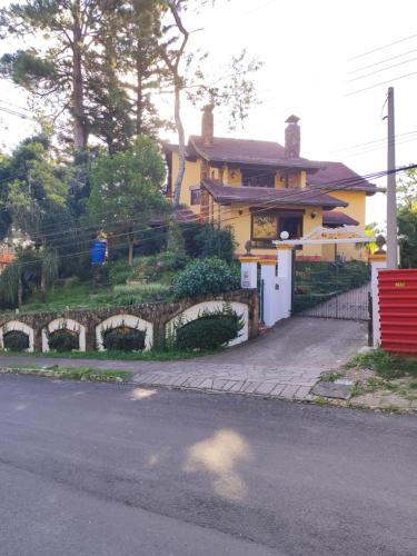 uma casa amarela com uma cerca de pedra ao lado de uma rua em Pousada Oscar Magic Gramado em Gramado