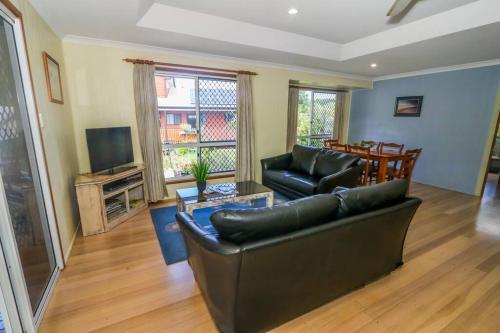 a living room with a leather couch and a television at McLeods - Three-Bedroom, Pet-Friendly Coastal Escape in Central Agnes Water in Agnes Water