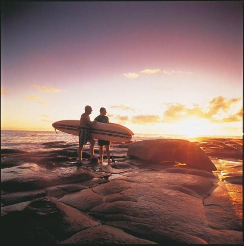 two people standing on a rock holding a surfboard at McLeods - Three-Bedroom, Pet-Friendly Coastal Escape in Central Agnes Water in Agnes Water