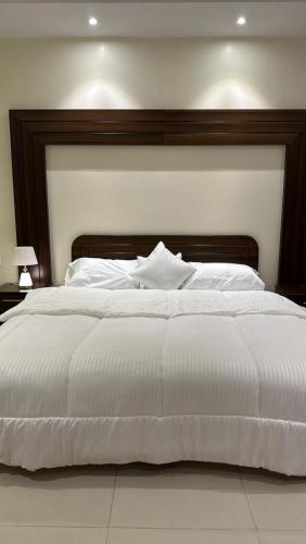 ein großes weißes Bett mit einem Kopfteil aus Holz in der Unterkunft شقه مفروشة فاخره بدخول ذاتي in Al Kharj