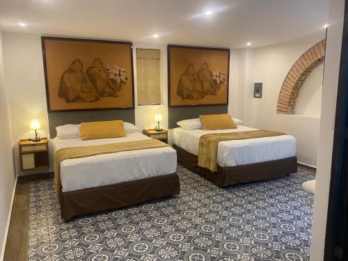 two beds in a hotel room with paintings on the walls at Hotel Tierra Marina Centro Historico in Mazatlán
