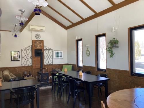 Pension Raclette في Nakafurano: غرفة طعام مع طاولات وكراسي ونوافذ