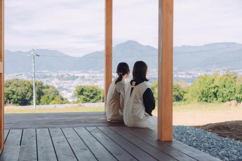 two women sitting on a porch looking out at the mountains at Cider Barn &more in Iida