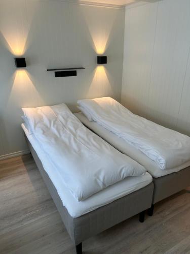 two beds in a room with white sheets and lights at Finsnes Gaard in Finnsnes
