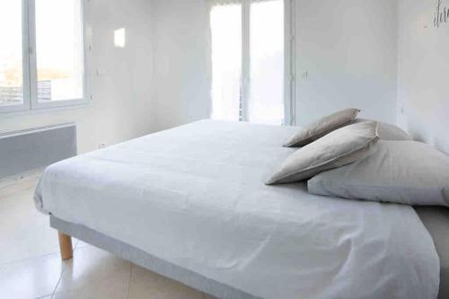 ein weißes Bett mit Kissen darauf im Schlafzimmer in der Unterkunft La Grande Croisée extérieur et plage in Châtelaillon-Plage