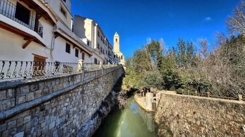 a stone wall next to a river with a building at Gaiamoment,com - Cueva las reinas in Alcalá del Júcar
