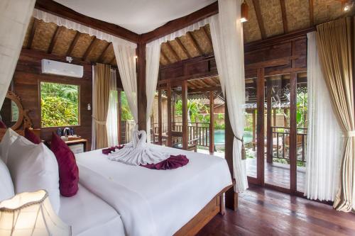a bedroom with a white bed in a room with windows at Tirta Jenar Villas in Tegalalang