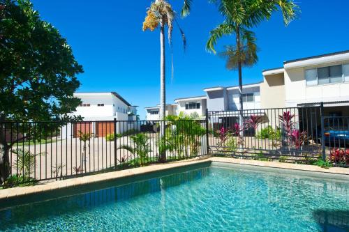 a swimming pool in front of a fence with palm trees at Magnetic Docks Townhouse 5 in Nelly Bay