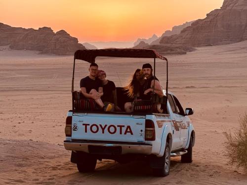 a group of people sitting in the back of a truck in the desert at Pink Desert Camp in Wadi Rum