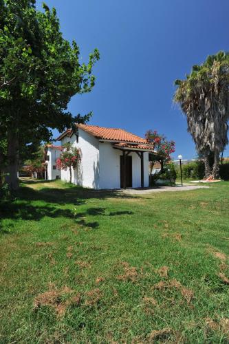 a white house with a tree and a grass field at Apartments Korakakis Beach in Finikounta