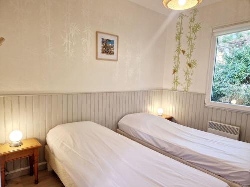 two beds in a room with two lamps and a window at Les Capucines in Portbail
