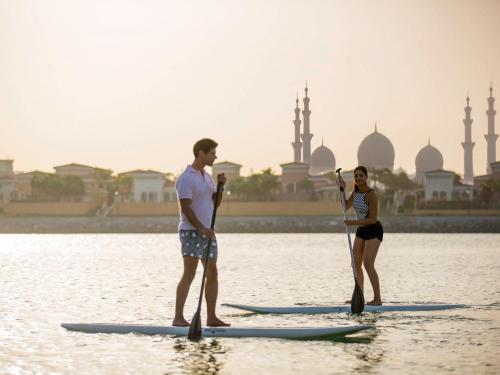 dos personas están de pie en tablas de paddle en el agua en Fairmont Bab Al Bahr, en Abu Dabi