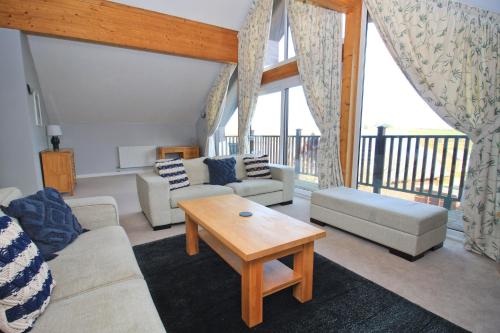 un soggiorno con divani, tavolo e balcone di Holiday lodge, on-site watersports, Retallack Resort a Saint Columb Major