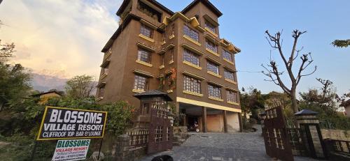 een groot gebouw met een bord ervoor bij Blossoms Village Resort in Dharamshala