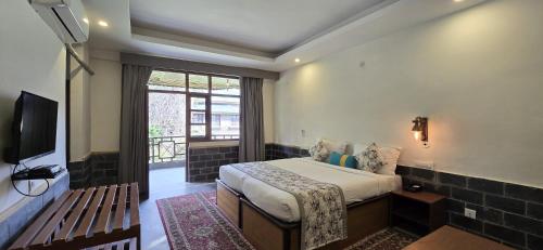 a bedroom with a bed and a tv and a window at Blossoms Village Resort in Dharamshala