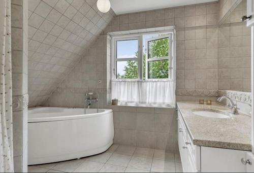 a bathroom with a tub and two sinks and a window at Nyere villa nær by, skov, strand in Højbjerg