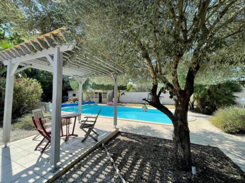 un patio con una mesa y un árbol junto a una piscina en Villa de 5 chambres avec piscine privee jardin clos et wifi a Saint Sulpice de Royan a 6 km de la plage, en Saint-Sulpice-de-Royan