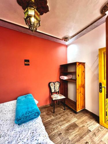 a bedroom with an orange wall with a bed and a chair at Riad Najiba in Rabat