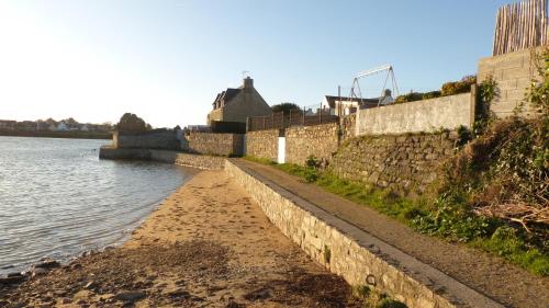 un mur en pierre à côté d'une masse d'eau dans l'établissement Appartement tout confort avec vue sur mer, à Plouhinec