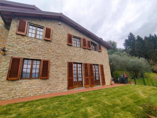 a stone house with brown shuttered windows and a yard at Villa Camelia Tuscany in Pescia