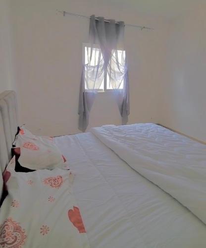 a bedroom with a large bed with white sheets and a window at Samira in Rufisque