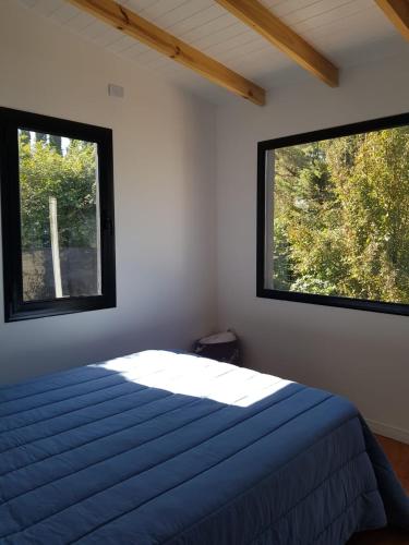 um quarto com duas janelas e uma cama com lençóis azuis em Atila de montaña em San Martín de los Andes