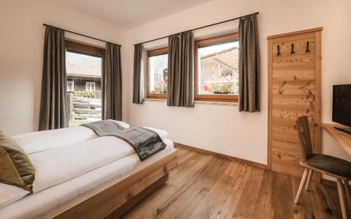 a bedroom with a bed and a tv and windows at Enzianhof - Nature Apartments in San Giovanni in Val Aurina