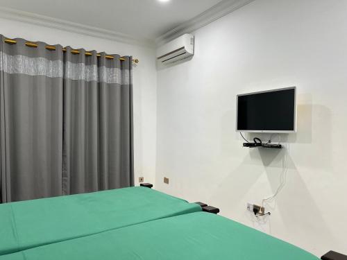 1 dormitorio con 1 cama verde y TV de pantalla plana en Empress Guest House en North Legon