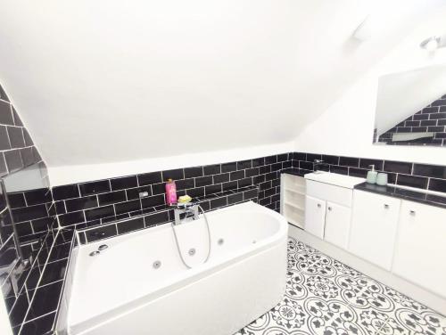 y baño con bañera blanca y azulejos negros. en Sigma Palace Free Parking en Longbenton
