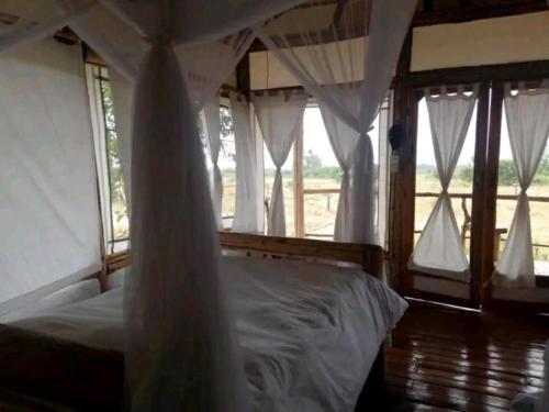 Schlafzimmer mit einem Bett mit weißer Bettwäsche und Fenstern in der Unterkunft Kazinga Wilderness Queen Elizabeth NP in Katunguru